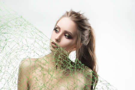 Beautiful naked shoulders young girl near her face diagonally stretched a green mesh of grass type veils. Isolated on white. Cosmetology, skin care. Copy space. Advertising, conceptual, commercial.の写真素材