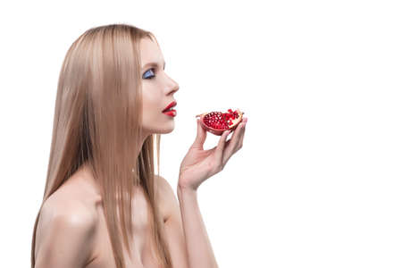Beautiful young long haired red lips blonde girl holds a half of pomegranate in her hands and smiles. Naked shoulders. Isolated on white. Copy space. Beauty, spa, health. Commercial, advertising.の写真素材
