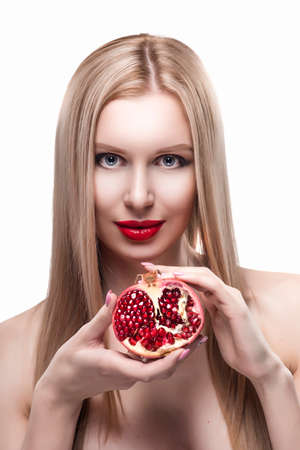 Beautiful young long haired red lips blonde girl holds a half of pomegranate in her hands and smiles. Naked shoulders. Isolated on white. Copy space. Beauty, spa, health. Commercial, advertising.の写真素材