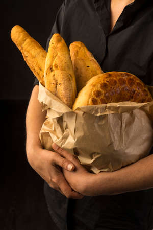 Conceptual art photography of a old woman hands hold different kinds of bread in a paper bag. Copy space. Advertising, cooking, bakery and commercial design.の写真素材