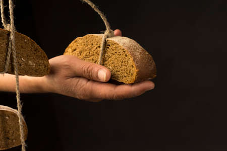 Conceptual art photography of a old woman hands holds pieces of bread hanging on the ropes, tied with twine. Copy space. Advertising, cooking, bakery and commercial design.の写真素材