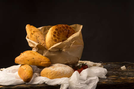 Conceptual still life art photography of a different kinds of bread wrapped in paper bag and cherry...