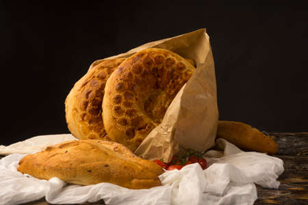 Conceptual still life art photography of a different kinds of bread wrapped in paper bag and cherry tomato branch on an ancient wooden table. Copy space. Advertising, cooking, bakery and commercial.の写真素材