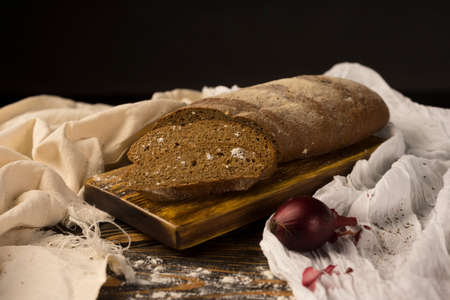 Conceptual still life of pieces of bread and two onion bulbs, on an ancient wooden table lying on a wooden tray, a piece of cloth. Copy space. Bakery, advertising and commercial design.の写真素材