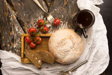 Conceptual still life of sliced bread, cherry tomatoes, glass of tea and vintage fork, on an ancient wooden table, and a piece of cloth. Copy space. Bakery, advertising and commercial design.の写真素材