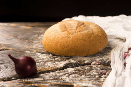 Conceptual still life of white bread and onion bulb, on an ancient wooden table, and a piece of cloth. Copy space. Bakery, advertising and commercial design.の写真素材