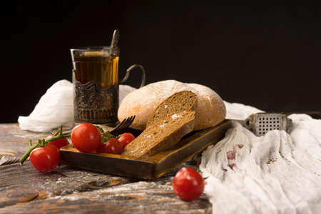Conceptual still life of sliced bread, cherry tomatoes, glass of tea and vintage fork, on an ancient wooden table, and a piece of cloth. Copy space. Bakery, advertising and commercial design.の写真素材