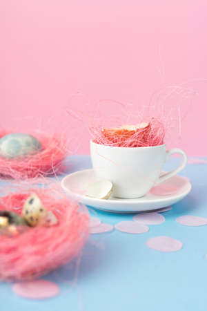 Yolk of broken egg in shell in a white coffee cup on a saucer, and blue chicken and quail eggs...