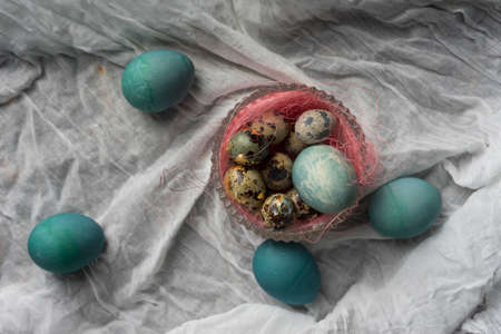 Several quail eggs in glass round vase decorated with a pink sisal and blue chicken eggs on white crumpled sackcloth. Copy space Advertising, commercial design.の写真素材