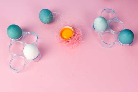 Yolk in eggshell decorated with pink sisal nest and several blue eggs in plastic egg boxes on the minimalist pink background. Copy space. Conceptual, commercial design.の写真素材