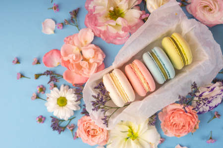 Multicolored macaroons cakes with big and small different flower buds in a gift box with wrapping paper on a blue background. Copy space. Bakery, cooking, gifts, conceptual and advertising.の写真素材