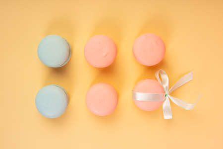 Blue and pink pastry macaroons, one of which is tied with a ribbon with a bow, arranged on a yellow background. Copy space. Bakery, cooking, conceptual and advertising design.の写真素材