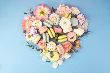 Multi Ñolored macaroons cakes with big and small different flower buds lay out in the shape of a heart on a blue background. Copy space. Bakery, cooking, gifts, conceptual and advertising.の写真素材