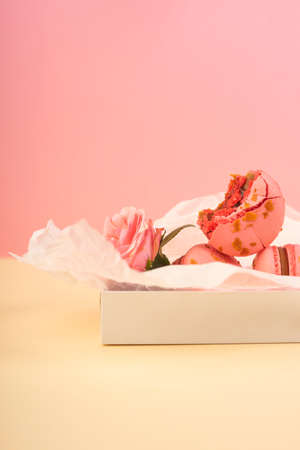 Several pink macaroons cakes one of which is bitten are placed in a gift box with wrapping paper...