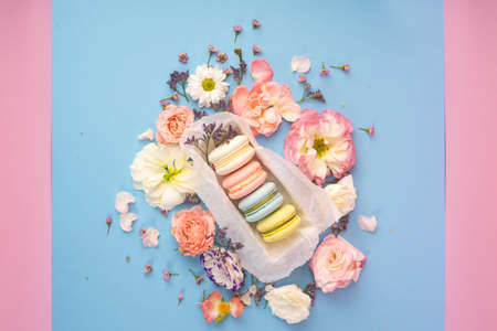 Multicolored macaroons cakes with big and small different flower buds in a gift box with wrapping paper on a blue and pink background. Copy space. Bakery, cooking, gifts, conceptual and advertising.の写真素材