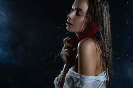 Beautiful wet naked shoulders slim girl wearing white wet shirt and sexy large cell black mesh pantyhose sensually holds old style phone in rain drops in theatrical smoke. Smooth wet skin. Copy spaceの写真素材