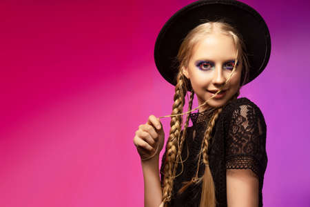 A beautiful smiling blonde teenage girl wearing a black gothic dress and a black hat. Conceptual...