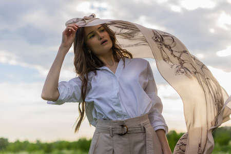 Beautiful stylish girl wearing a trendy white shirt, beige trousers and a pareo poses outdoors...