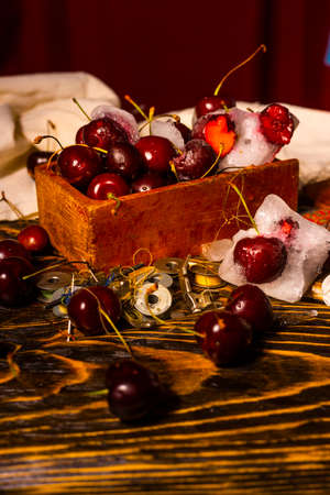 Frozen iced and fresh red cherry in a glass next to a vintage wooden box on an ancient wooden table on which spools of thread are scattered. Conceptual close-up photo. Copy space. Advertisement designの写真素材