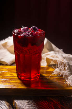 Frozen icy red berries in a glass on crumpled wrapping paper standing on a vintage wooden table. Conceptual close-up photo.Copy space. Advertisement and commercial designの写真素材