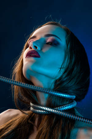 Beautiful brunette girl with dark red lips make-up, pulls a metal shower spiral hose wrapped around her neck. Conceptual, fashionable, technology and advertising design.の写真素材