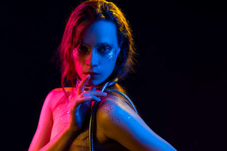 Beautiful girl with cretative make-up made of glitter with tears on her face wraps her neck with a...