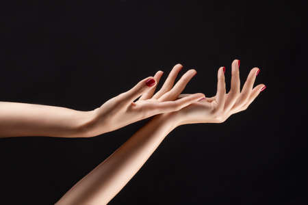 Closeup of beautiful woman hands with red manicure on the nails. Cream for palms, manicure and beauty treatment. Elegant and graceful arms with slender graceful fingers. Copy space. Isolated on black.の写真素材