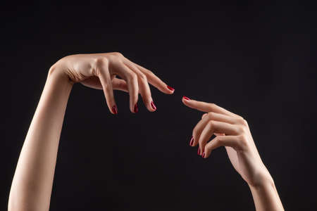 Closeup of beautiful woman hands with red manicure on the nails. Cream for palms, manicure and beauty treatment. Elegant and graceful arms with slender graceful fingers. Copy space. Isolated on black.の写真素材