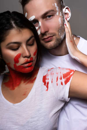 Beautiful couple of artists wearing jeans and white t-shirts soiled with white and red paint...
