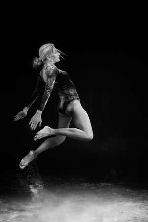 Beautiful slim girl wearing a gymnastic bodysuit covered with clouds of the flying white powder...