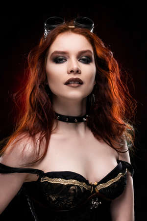Beautiful smiling redhead cosplayer girl wearing a Victorian-style steampunk costume with a big breast in a deep neckline on red and black background. Portrait. Copy space.の写真素材