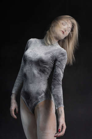 Beautiful slim girl wearing a black gymnastic bodysuit covered with white powder talcum dust jumps dances on a dark. Artistic conceptual and advertising photo. Copy spaceの写真素材