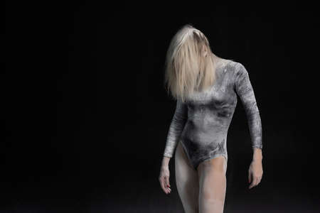 Beautiful slim girl wearing a black gymnastic bodysuit covered with white powder talcum dust jumps dances on a dark. Artistic conceptual and advertising photo. Copy spaceの写真素材