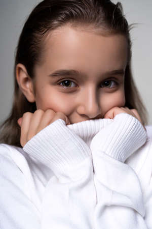 Portrait of a cute smiling teen girl wearing a white turtleneck sweater. Isolated on gray...