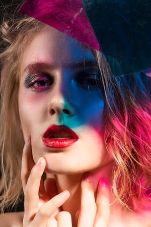 Close-up face of a beautiful young blonde girl with red lips and her face is covered with colored shadows from multi colored pieces of transparent plastic. Fashion, commercial and conceptual design.の写真素材