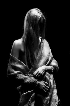 Beautiful young slim busty and leggy naked blonde model girl, sensually covering her nudity with a burlap cloth. Dark background. Conceptual artistic black and white photo.の写真素材