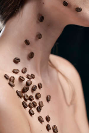 Beautiful girl with naked shoulders. Coffee beans were artistically stuck to the healthy clean skin of her face and neck. Advertising and commercial design. Close up. Copy space.の写真素材