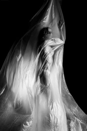 Slim girl dressed only in underwear emotionally posing, wrapped in fluttering in the wind and fitting her graceful young body cellophane film. Artistic, creative, abstract design. Black and white.の写真素材