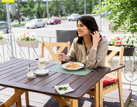 Beautiful smiling brunette girl having lunch in a street cafe, sitting at a table and eating Italian pasta. Advertising, commercial design. Copy space.の写真素材
