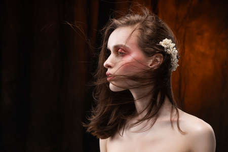 A beautiful slim girl with naked shoulders and fashionable red makeup, wearing jewelry in her hair,...