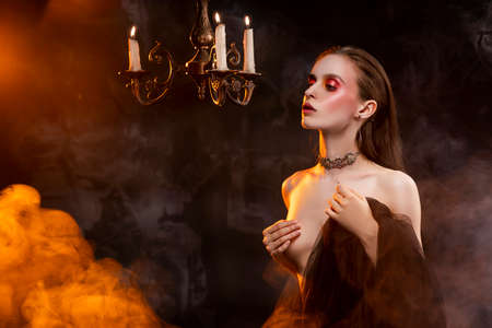 A beautiful slim topless girl, wearing earrings and a necklace, and covering her nudity with a black...