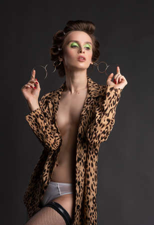 A beautiful topless girl wearing a stockings, and an unbuttoned leopard blouse pulls earrings with her fingers. Fashionable, advertising designの写真素材