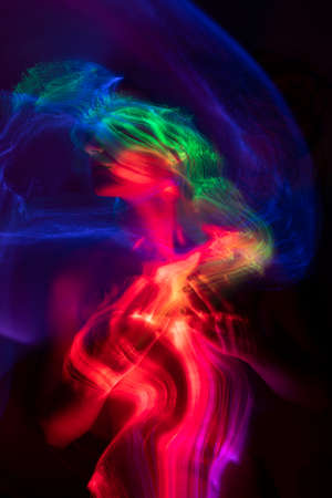 Conceptual avant-garde portrait of a beautiful young girl covered with multicolored lines applied by a light brush. Art style creative photo. Advertising, fashion and commercial designの写真素材