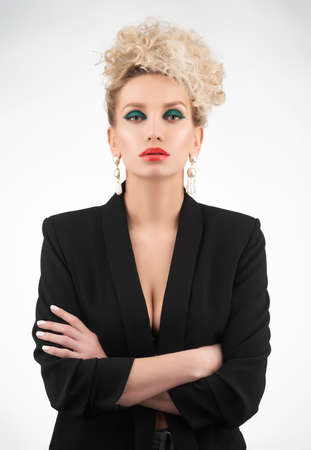 A beautiful blonde girl with an elegant hairstyle and large breasts, wearing a bra, trousers and a blazer, poses isolated on white. Trendy, commercial and advertising designの写真素材
