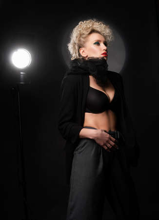 A beautiful blonde girl with an elegant hairstyle and large breasts, wearing a bra, trousers, scarf and a blazer, fashinable poses near the spotlight. Trendy, commercial and advertising designの写真素材
