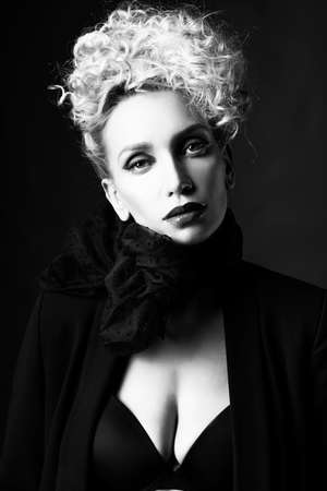 A beautiful blonde girl with an elegant hairstyle and large breasts, wearing a bra, scarf and a blazer, poses in the dark. Trendy,monochrome, black and white, noir design. Close Up portraitの写真素材