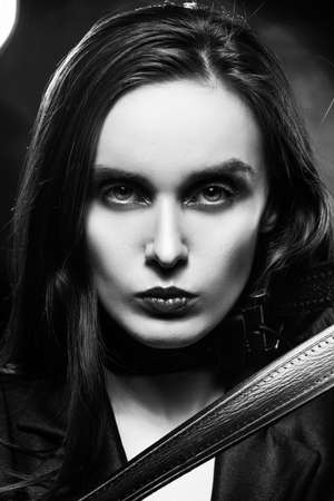 Braless girl with red lips, wearing a unbuttoned blazer and a leather belt tightened around the neck, which she pulls with her hands,  on the dark background, next to a light lamp. Monochrome designの写真素材