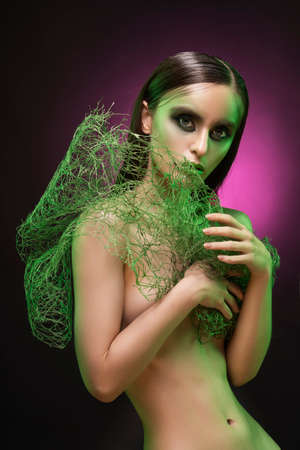 A beautiful slim topless girl with  makeup covers her breast with green net on a black and pink background. Artistic, fashionable, advertising designの写真素材