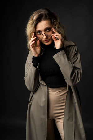 Beautiful girl wearing a casual trendy trousers, turtleneck glasses and raincoat posing on a dark background. Fashionable, advertising, lifestyle and commercial designの写真素材