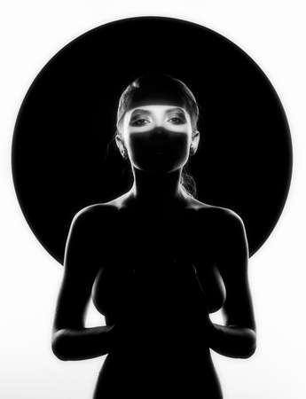 Beautiful topless busty girl poses at the black circle. Her breast and face is hide in the deep shadows and seen only her body silhouette and her eyes. Isolated on white. Artistic monochrome designの写真素材